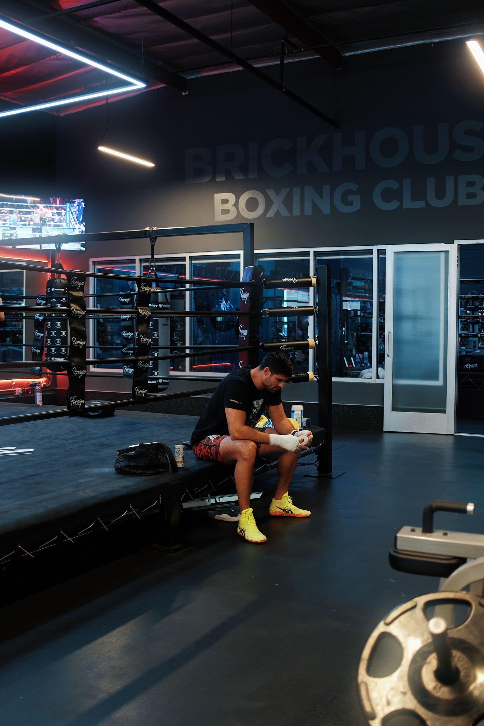 Andrii Novytskyi wrapping his hands seated on the ring apron under red gym light